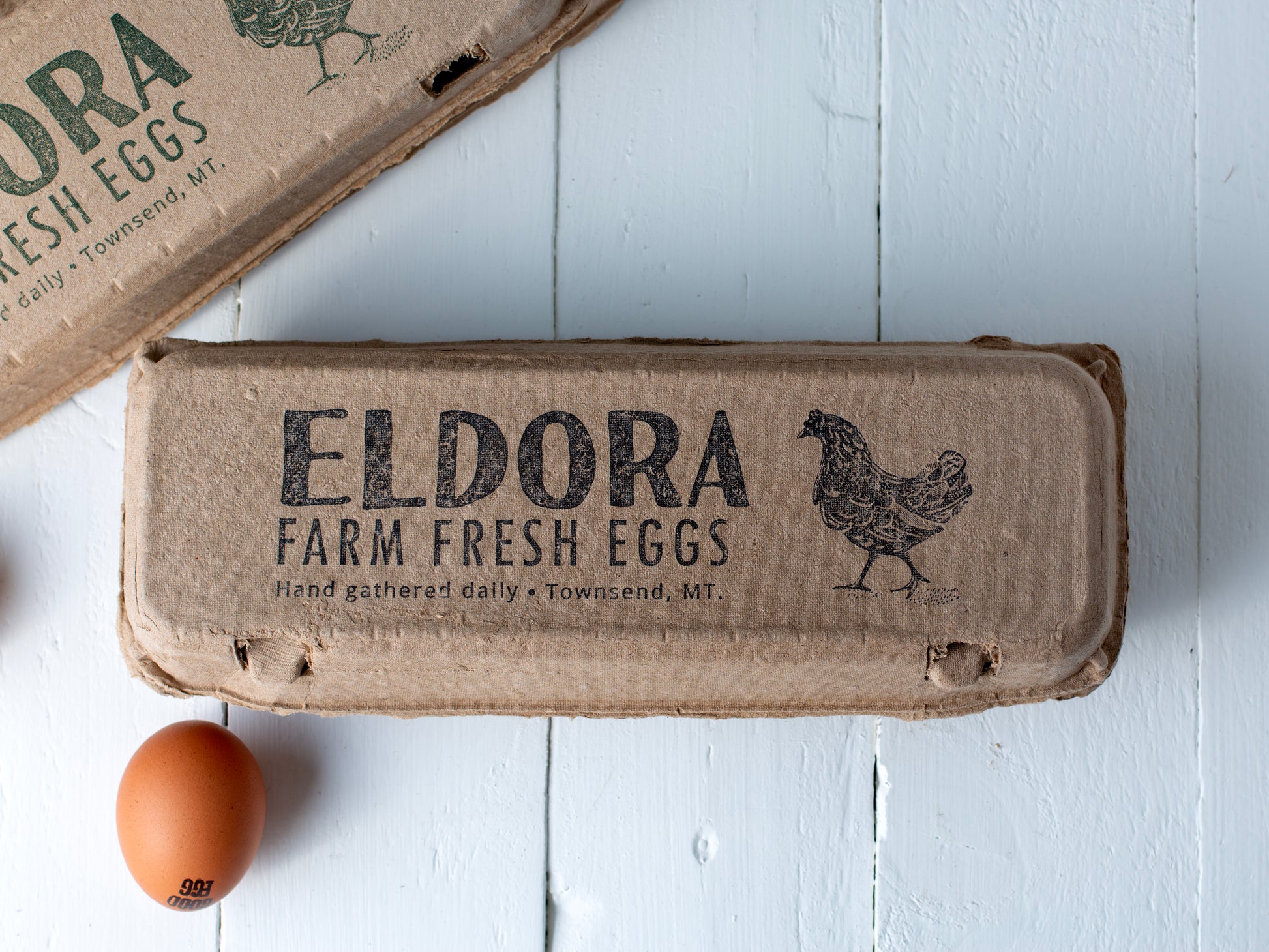 wide lid branding stamp on kraft egg carton; black ink wordmark with chicken icon; product label placement across top.